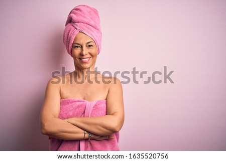 Middle age woman wearing bath towel from beauty body care over pink background happy face smiling with crossed arms looking at the camera. Positive person.