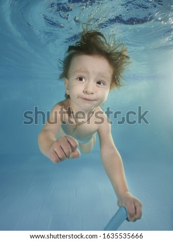 Funny red-haired boy plays with toy underwater in a swimming pool