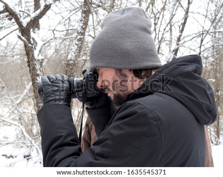 Portrait of a young man with a camera taking pictures in a forest preserve in winter
