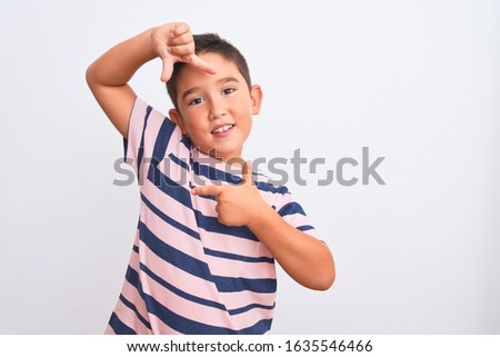 Beautiful kid boy wearing casual striped t-shirt standing over isolated white background smiling making frame with hands and fingers with happy face. Creativity and photography concept.