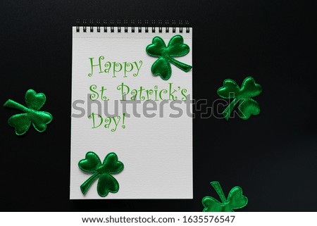 St. Patrick’ Day greeting card with text and shamrock leaves on black background.