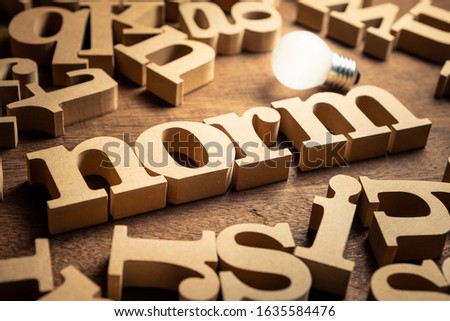 NORM word by wood alphabets with many random letters around and glowing light bulb Royalty-Free Stock Photo #1635584476