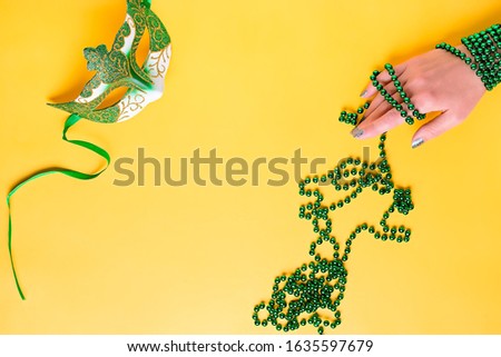 Mardi gras accessories flat lay on bright yellow background, top view, copy space. Woman holding carnival mask and beads. Festival holiday concept overhead