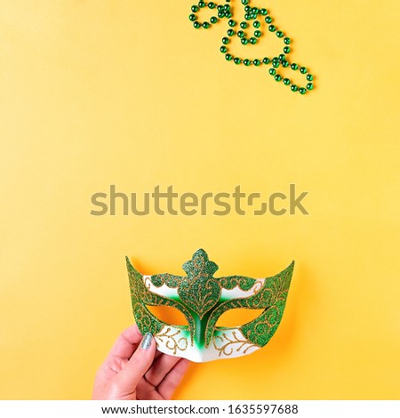 Mardi gras accessories flat lay on bright yellow background, top view, copy space. Woman holding carnival mask and beads. Festival holiday concept overhead