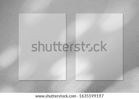 Two empty white vertical rectangle poster or business card mockups with diagonal dappled light spots on gray concrete wall. Flat lay, top view. For advertising, brand design, stationery presentation.