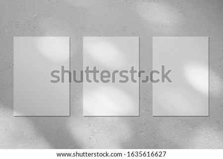 Three empty white vertical rectangle poster or business card mockups with diagonal dappled light spots on gray concrete wall. Flat lay, top view. For advertising, brand design, stationery presentation Royalty-Free Stock Photo #1635616627