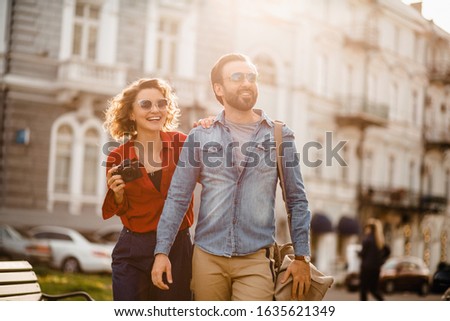attractive smiling man and woman traveling together sightseeing, stylish couple in love taking pictures on digital camera on romantic trip, sunny summer city, travelers in sunglasses having fun