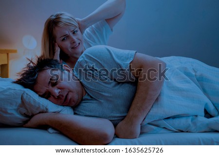 Married couple lying in bed. Woman trying to wake up husband who is snoring and covering her ears with her hands. Annoyed upset wife trying to sleep with snoring husband asleep next to her Royalty-Free Stock Photo #1635625726