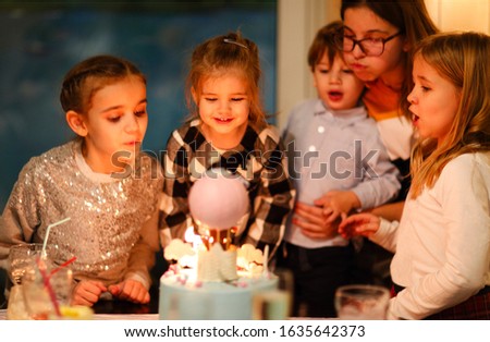 Group of joyful little kids celebrating birthday party and blowing candles on cake. Birthday concept

