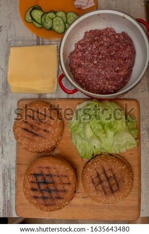 cooking hamburgers, making a hamburger, pictures with buns, raw meat, cheese and vegetables on the table. rolls and minced meat for making burgers and cheese. Iceberg lettuce leaves. Minced beef
