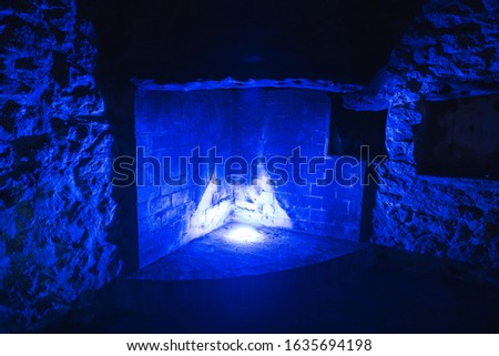 Interior of a brick building with an empty fireplace with blue light illuminating the entire space