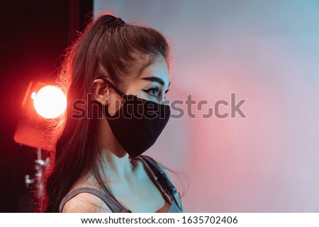 A beautiful brunette amid red-blue light in a black mask on her face that protects against the virus, the coronavirus