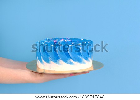 Girl's hands are holding beautiful and tasty cake with white and true blue color cream on a blue background with place for text.