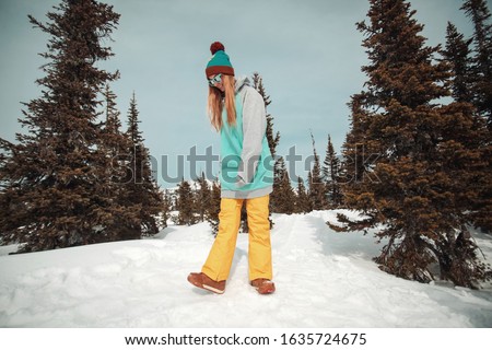 Beautiful girl dressed in hoodie and hat, wear sunglasses, posing in front sky in spruces in winter day