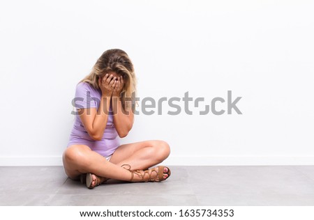 young pretty latin woman feeling sad, frustrated, nervous and depressed, covering face with both hands, crying sitting on the floor