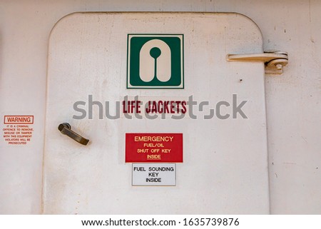 Close up of the door of the life jacket compartment room on a passenger ferryboat in Canada. White aged surface with signs with explicative icons.