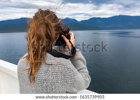 Young woman photographer shot from behind while taking pictures from the deck of a ferry. Expensive photographic equipment and long telephoto lens.