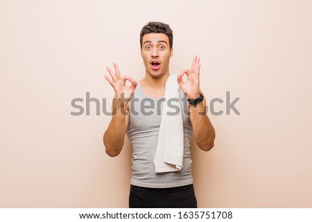 young arabian man feeling shocked, amazed and surprised, showing approval making okay sign with both hands. sport concept