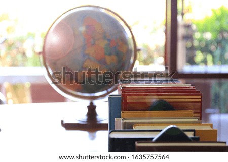 Backlit of many books arranged in rows on the library desk. Globe as background selective focus and shallow depth of field