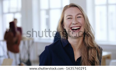 Happy blonde business woman in formal clothes posing, laughing and smiling cheerfully at trendy modern office workplace.