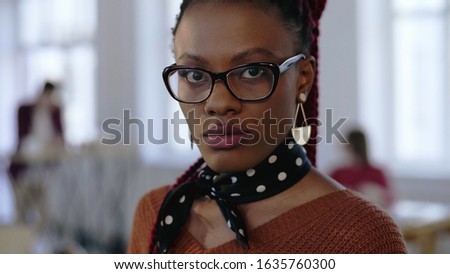 Close-up portrait of young beautiful serious black business woman in eyeglasses looking at camera at office workplace.
