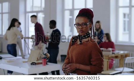 Portrait of young African business woman in eyeglasses posing serious and stressed, then smiling at trendy loft office.