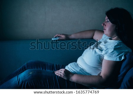 Laziness, sedentariness, overweight, daily routine, television addiction. Woman sitting at coach watching TV late at night