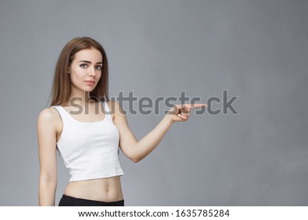 Beautiful girl shows finger to the side of copy space and standing on gray background. lot of free 
space.