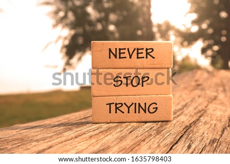 Motivational and creative concept: Wooden blocks arranged with words NEVER STOP TRYING at outdoor with natural lights, selective focus 