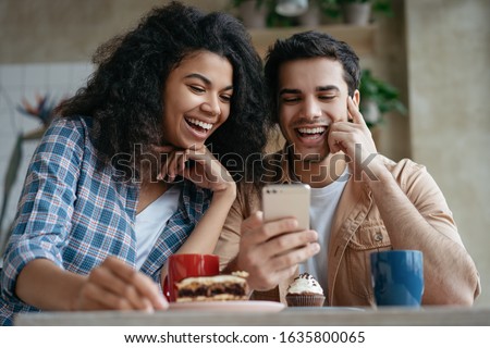 Happy couple using mobile phone and internet, watching movie together, communication, laughing, sitting in cafe. Positive hipster friends shopping online, looking at digital screen  Royalty-Free Stock Photo #1635800065