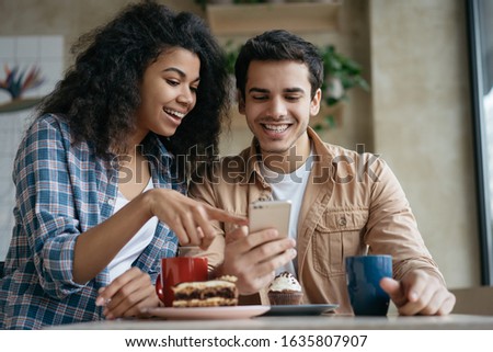 Happy couple using mobile phone application for online shopping. Emotional friends communication, laughing, looking at digital screen, sitting together in cafe  Royalty-Free Stock Photo #1635807907