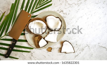 Healthy nutritious natural coconut with a vast range of dietary and cosmetic uses, shown here with coconut cut into pieces on marble table top, creative flat lay layout overhead. Negative copy space.
