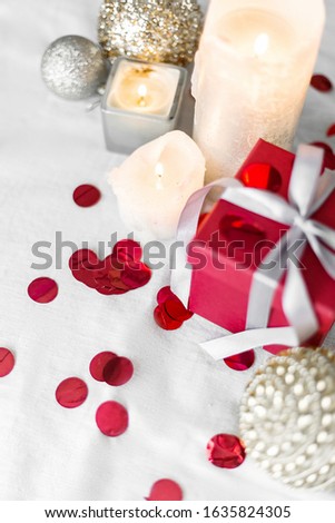 New year and Christmas card, colorful red and silver baubles with a gift box, candles and confetti on a white background. selective focus. top view