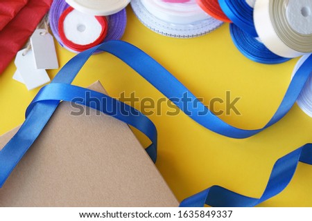 Gift box packaging on a yellow background. A lot of bright satin ribbons.