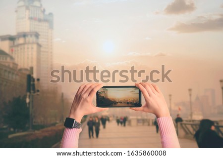 Shot of woman hand with a mobile phone to shoot a video While traveling in a large city under the sunlight.