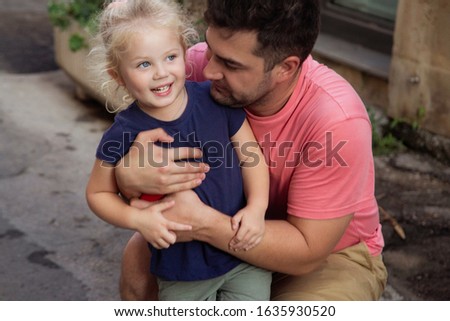 Father and his daughter, blonde little cute  child, are fishing  on the lake in summer sunny day. They are sit at the wooden pier and hugging and smiling.
