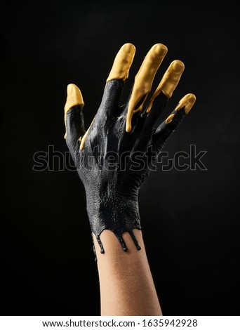 Female refined hand smeared with black and gold acrylic paint on a black background
