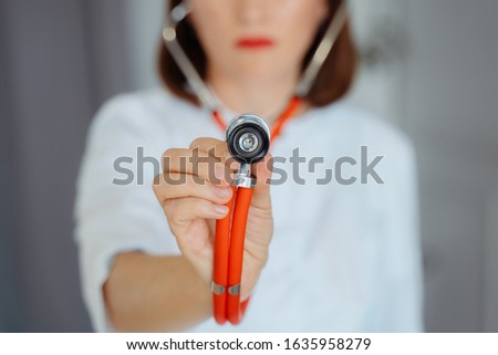 Female doctor in a white coat holds a stethoscope.