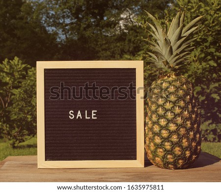 Fresh Pineapple outdoors with summer sale signboard, garden in background