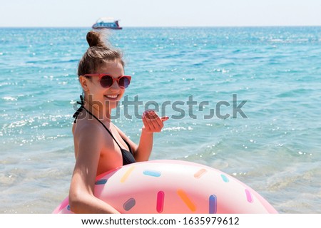 Fit woman with donut inflatable ring is calling to join her swimmimg in the sea.