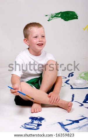 A smiling young boy is enjoying painting pictures.