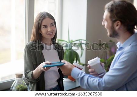 Sharing pictures. A woman taking a tablet from a man while drinking coffee