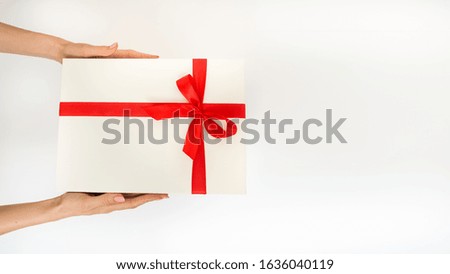 Top view of female hands holding a gift box white with a red ribbon, one object on a white background with free space for text
