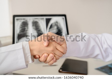 Close up picture of  doctors shaking hands in hospital. Background with chest x-ray. Free space for text
