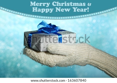 Female hands  in mittens with gift box, on color background