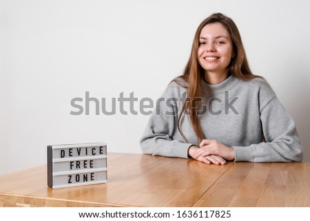 Happy girl sitting relaxed at the table with sign device free zone. Digital detox concept