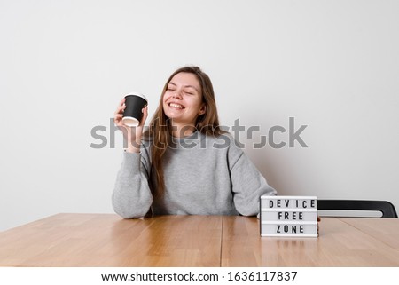 Happy girl sitting relaxed at the table with sign device free zone. Digital detox concept
