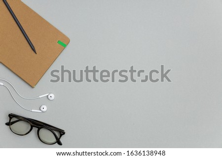 Blank notebook, earphones, glasses on gray background.
