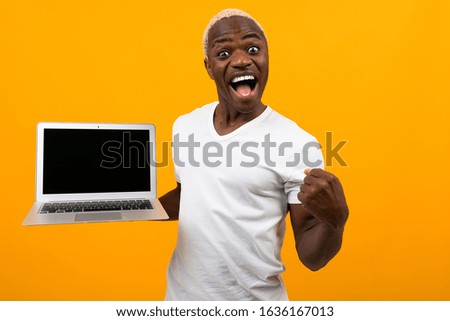 joyful black american man with a beautiful snow-white smile in a white t-shirt with a laptop with a layout on an orange studio background