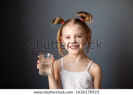 little cute girl drinks water from a glass on a gray background
